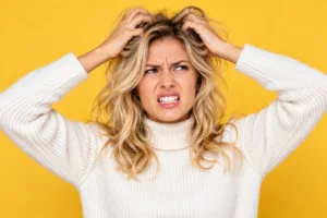 Prurito in testa Donna che si gratta la testa con entrambe le mani: prurito al cuoio capelluto, cause e rimedi